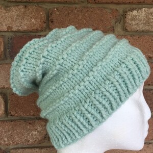 Pode incluir: Um gorro de malha de cor verde claro com um ajuste folgado. O gorro &eacute; feito com um padr&atilde;o de ponto texturizado.