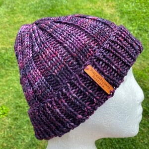 May include: Purple and pink knitted beanie with a brown leather tag that reads "Stacey's Knits Australia".