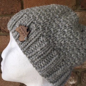 May include: Gray knitted beanie with a wooden tag that says "Handmade with love in the UK".