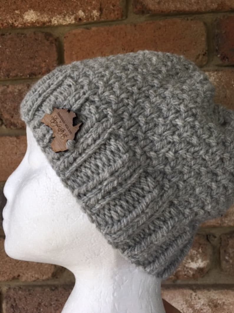May include: Gray knitted beanie with a wooden tag that says "Handmade with love in the UK".