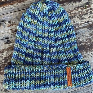 May include: A blue, green, and grey knitted beanie with a brown leather tag that reads "Stacysknits Australia".
