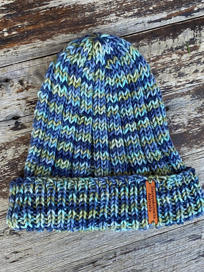 May include: A blue, green, and grey knitted beanie with a brown leather tag that reads "Stacysknits Australia".