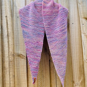 May include: A triangular knit scarf featuring a variegated color palette of pink, purple, blue, and orange yarn. The scarf is constructed with a garter stitch pattern and includes a small brown leather tag attached to one of the bottom points.