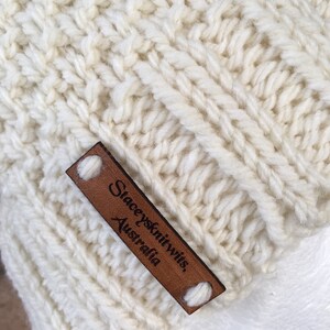 May include: A close-up of a white knitted hat with a brown leather label that reads "Staceyknits, Australia".