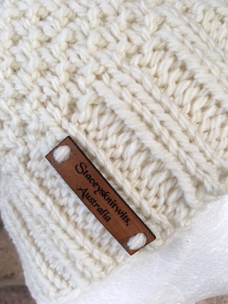 May include: A close-up of a white knitted hat with a brown leather label that reads "Staceyknits, Australia".