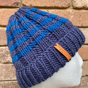 May include: A dark blue knitted beanie with blue stripes and a brown leather tag that reads "Stacey's Knits Australia".