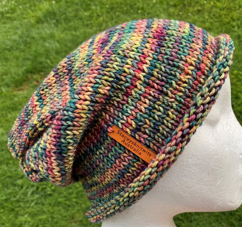 May include: Multicolored knitted beanie hat with a brown leather tag that reads "Stacey's Knitwits Australia".