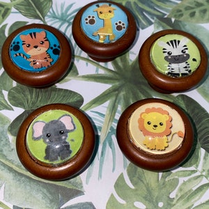 May include: Five wooden knobs with colorful animal illustrations. The knobs feature a giraffe, tiger, zebra, elephant, and lion. The knobs are perfect for adding a touch of whimsy to any room.