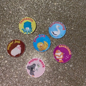May include: Six colorful round stickers with animal illustrations and positive messages. The stickers feature a duck, a sheep, a koala, an octopus, a fish, and a goose. The messages on the stickers include "super job", "good job", "super work", "fantastic", "excellent", and "outstanding".