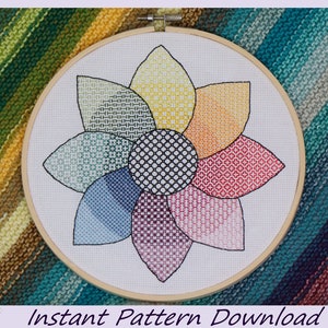 May include: A colorful cross-stitch pattern of a flower with eight petals, each petal is a different color and pattern. The flower is in a wooden embroidery hoop.