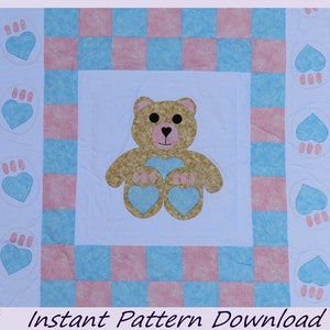 Può includere: Una trapunta per neonati con un orsacchiotto marrone al centro. La trapunta è realizzata con quadrati rosa e blu con un bordo bianco. Il bordo è decorato con cuori blu e impronte di zampe.