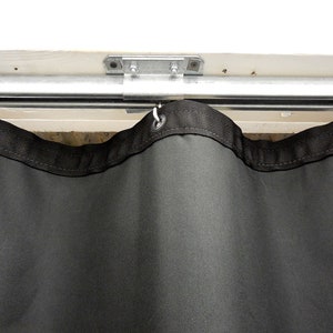 May include: Black soundproof curtain with grommets hanging from a metal track. The curtain is made of a thick, durable fabric.