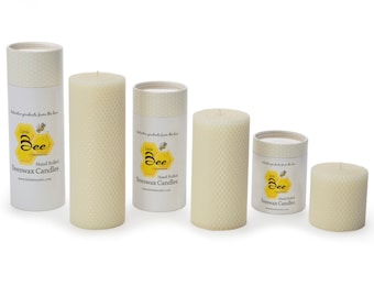 Op de afbeelding: Vier handgerolde bijenwaskaarsen in verschillende maten in een natuurlijke crèmekleur. De kaarsen zitten in hun verpakking, die een honingraatpatroon en de tekst "Little Bee Candles" heeft.