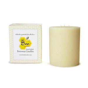 Op de afbeelding: Een handgerolde bijenwaskaars in een cilindrische vorm met een honingraatpatroon. De kaars is wit en heeft twee lonten. De kaars is verpakt in een doos met een geel en wit honingraatpatroon en de tekst "Little Bee Candles" en "Hand Rolled Beeswax Candles".