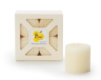 Op de afbeelding: Een doos met zes handgerolde bijenwas-theelichtjes. De kaarsen zitten in een witte doos met een honingraatpatroon en een geel label met de tekst "Little Bee Candles" en "Hand Rolled Beeswax Votives".