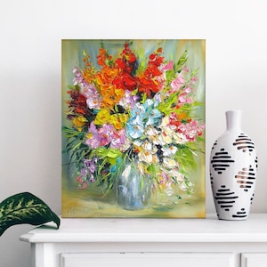 May include: A painting of a colorful bouquet of flowers in a vase. The flowers are mostly pink, red, yellow, and white. The vase is a light gray color and is sitting on a green surface. The background is a light green color.