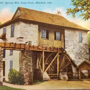 May include: A vintage postcard depicting a stone watermill with a wooden water wheel. The mill is surrounded by trees and a wooden bridge. The text on the postcard reads "Hamer's Mill, Spring Mill State Park, Mitchell, Ind."
