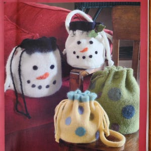 May include: Image of handmade drawstring bucket bags. The bags are made of felt and feature snowman and polka dot designs. The bags are white, yellow, and green with black, orange, and blue accents. The text "INDYGO JUNCTION" and "DRAWSTRING BUCKET BAG" are visible.
