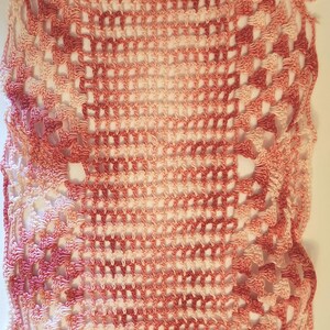 May include: A crocheted doily with a pink and white ombre design. The doily is square shaped and has a delicate lace pattern.