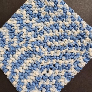 May include: A blue and white crocheted dishcloth or pot holder. The cloth is made with a textured stitch and has a square shape.