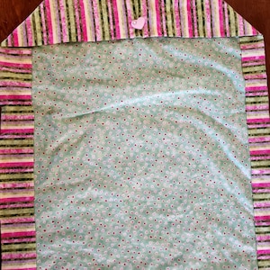 May include: A green fabric table runner with a pink and green striped border. The runner is decorated with a small white heart button and a pattern of tiny red hearts on a light green background.