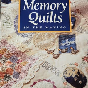 May include: A softcover book titled Memory Quilts In The Making by Leisure Arts. The cover features a cream-colored quilt decorated with various fabric patches, including lace doilies, embroidered chickens, a house, and handwritten notes.
