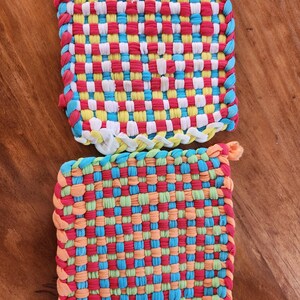 May include: Two colorful woven pot holders, one with red, yellow, white, and blue stripes, and the other with red, orange, green, and blue stripes.