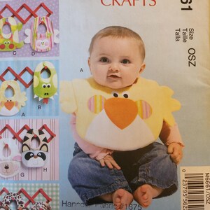 May include: A baby wearing a yellow bib with an orange beak and colorful accents. The image is a McCall's Crafts pattern, featuring various bib designs with animal faces, including a frog, raccoon, and giraffe.