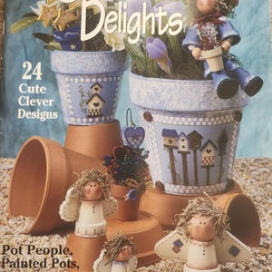 May include: A book titled "Garden Delights" with 24 cute and clever designs for painted flower pots, plant pokes, and pot people. The cover features a blue and white painted flower pot with a birdhouse design, a small angel figurine, and a girl figurine holding a flower pot.