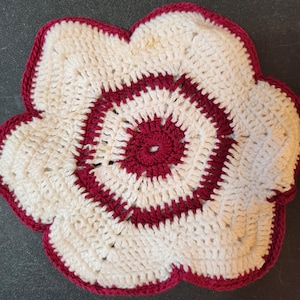 May include: A handmade, crochet flower-shaped trivet. The trivet features a white center with a deep red spiral design and a matching red scalloped edge. This decorative item is likely used to protect surfaces from hot dishes.