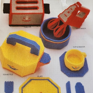 May include: A collection of handmade, colorful, and textured toy kitchen items. The set includes a yellow tea kettle, plate, cup and saucer, and a red hand mixer. Also included are a toaster, knife, fork, and spoon.