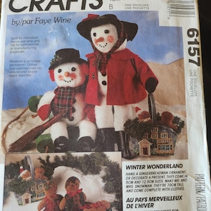 May include: A McCall's Crafts sewing pattern envelope 6157 by Faye Wine featuring illustrations of two snowmen figures, one standing and one sitting on a sled, alongside gingerbread man ornaments and a small bakery-themed basket.