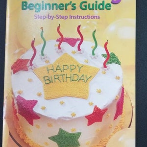 May include: A cake decorating guide for beginners. The cover features a decorated birthday cake with candles, stars, and the words "Happy Birthday." The book is published by Wilton Enterprises.