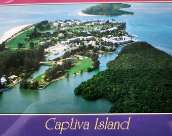 May include: An aerial view of Captiva Island, Florida. The image shows a lush green island with a network of waterways and a sandy beach. The island is surrounded by clear blue water.