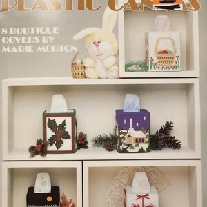 May include: A craft project leaflet showing eight different tissue box covers in plastic cans. The covers are decorated with holiday themes, including a bunny, a basket of eggs, holly, a church, a pumpkin, a cat, a heart, and a bow. The leaflet is titled "Holiday Tissue Covers in Plastic Cans" and is numbered 333. The price is $2.50.