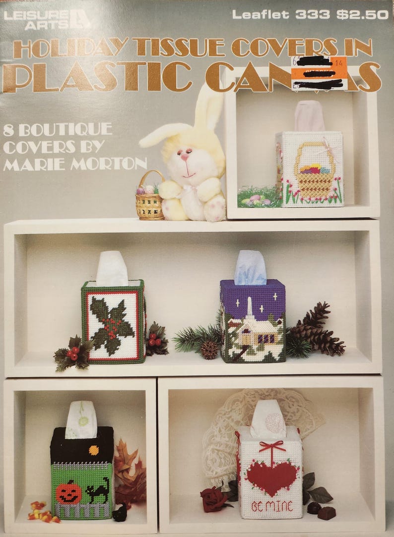 May include: A craft project leaflet showing eight different tissue box covers in plastic cans. The covers are decorated with holiday themes, including a bunny, a basket of eggs, holly, a church, a pumpkin, a cat, a heart, and a bow. The leaflet is titled "Holiday Tissue Covers in Plastic Cans" and is numbered 333. The price is $2.50.