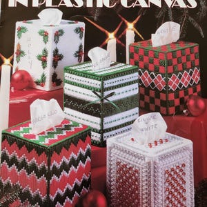 May include: A Leisure Arts craft leaflet titled Festive Boutiques in Plastic Canvas, featuring four square tissue box covers. Designs include holly, ribbon, argyle, bargello, and silver-white patterns in red, green, white, and black colors.