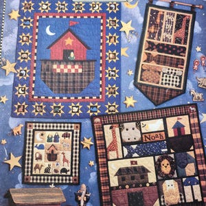 May include: A collection of four colorful quilt patterns featuring a Noah's Ark theme. The quilts are framed and displayed against a blue background with stars. The quilts feature a variety of animals, including giraffes, lions, and owls. The text "Noah" and "Two by Two" are visible on the quilts.