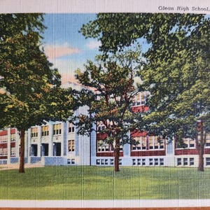 May include: A vintage postcard depicting Olean High School in Olean, New York. The school building is a two-story brick structure with large windows and a central entrance. The building is surrounded by lush green trees.