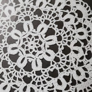 May include: A white, circular doily with an intricate crochet design. The doily features a repeating floral pattern with openwork details, creating a delicate and lacy appearance. The edges are scalloped, adding to its decorative appeal. This handmade item is suitable for home decor.