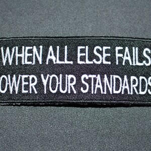 May include: Black embroidered patch with white text that reads "When all else fails lower your standards!"