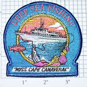May include: A blue embroidered patch with the text "Deep Sea Fishing" and "Miss Cape Canaveral". The patch features a white boat with a pink fish and a blue marlin in the water.