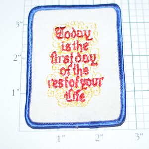 May include: A white embroidered patch with blue edging. The text reads "Today is the first day of the rest of your life".