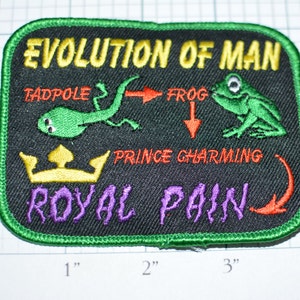 May include: A green, black, and yellow embroidered patch with the text "Evolution of Man" and images of a tadpole, frog, and a crown. The text "Prince Charming" and "Royal Pain" are also included.