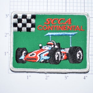 May include: A green embroidered patch with a white border featuring a checkered flag, a race car, and the text "SCCA CONTINENTAL".