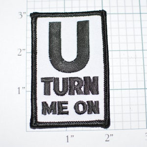May include: A black and white embroidered patch with the letter "U" and the text "TURN ME ON" in a black font.
