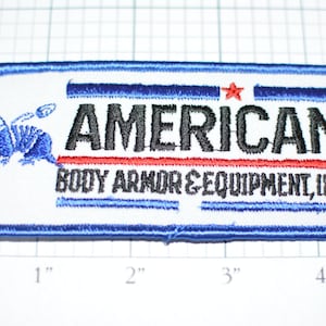 May include: A white embroidered patch with blue trim. The patch features a black and blue armadillo, a red and blue stripe, and the text "AMERICAN BODY ARMOR & EQUIPMENT, INC."