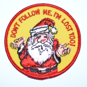 May include: A yellow and red embroidered patch with a cartoon Santa Claus. The text on the patch reads "Don't follow me, I'm lost too!"