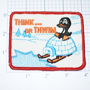 May include: A white embroidered patch with a red border. The patch features a cartoon penguin wearing a red hat and riding a snowmobile. The text "THINK... OR THWIM" is embroidered in orange on the patch.