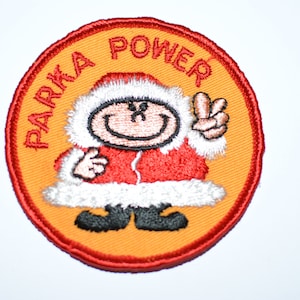May include: A round, orange and red embroidered patch with a cartoon character wearing a red and white parka and holding up a peace sign. The text "Parka Power" is written around the character.